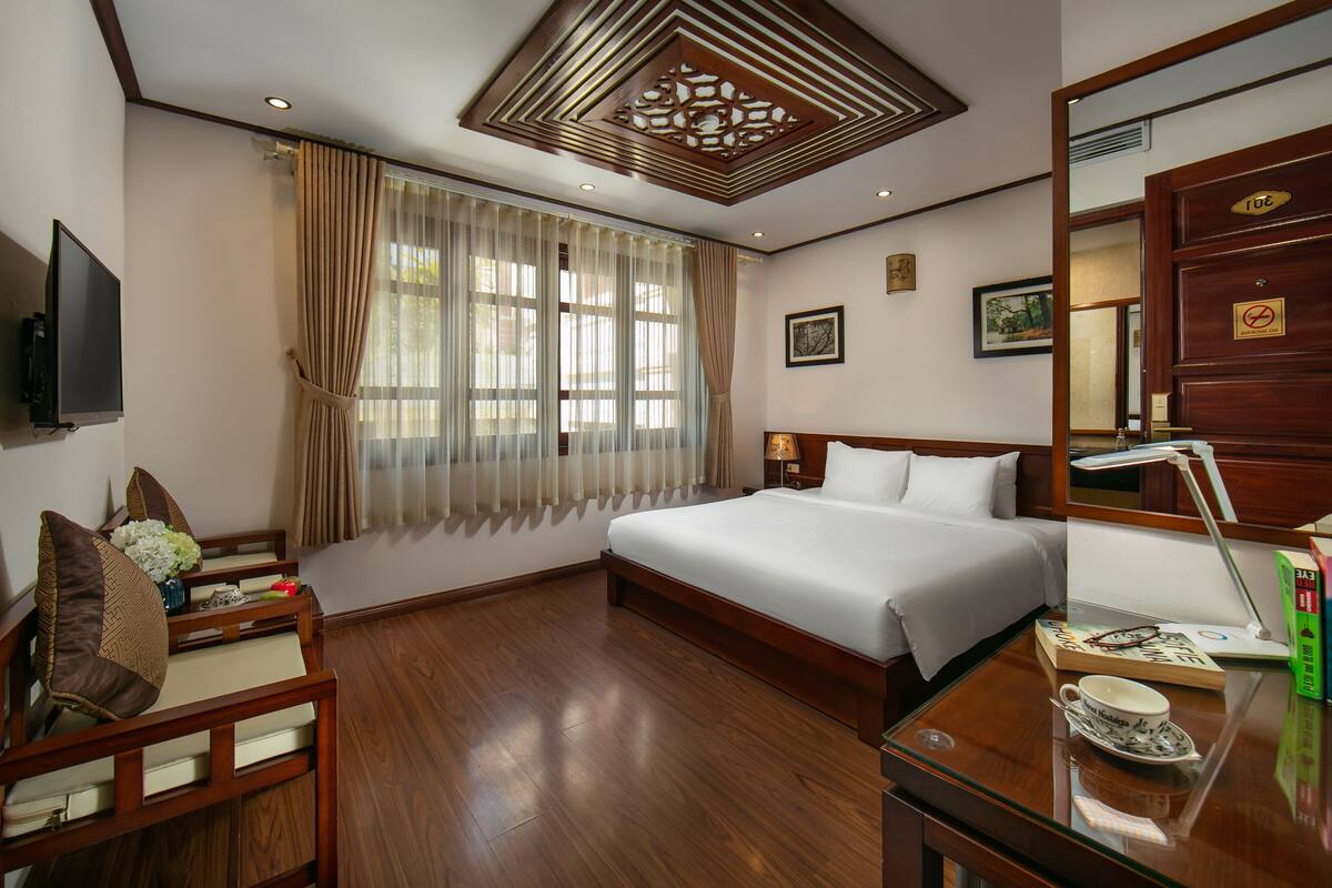 A hotel room with a large bed, a desk with a lamp, a television, and a window with curtains.