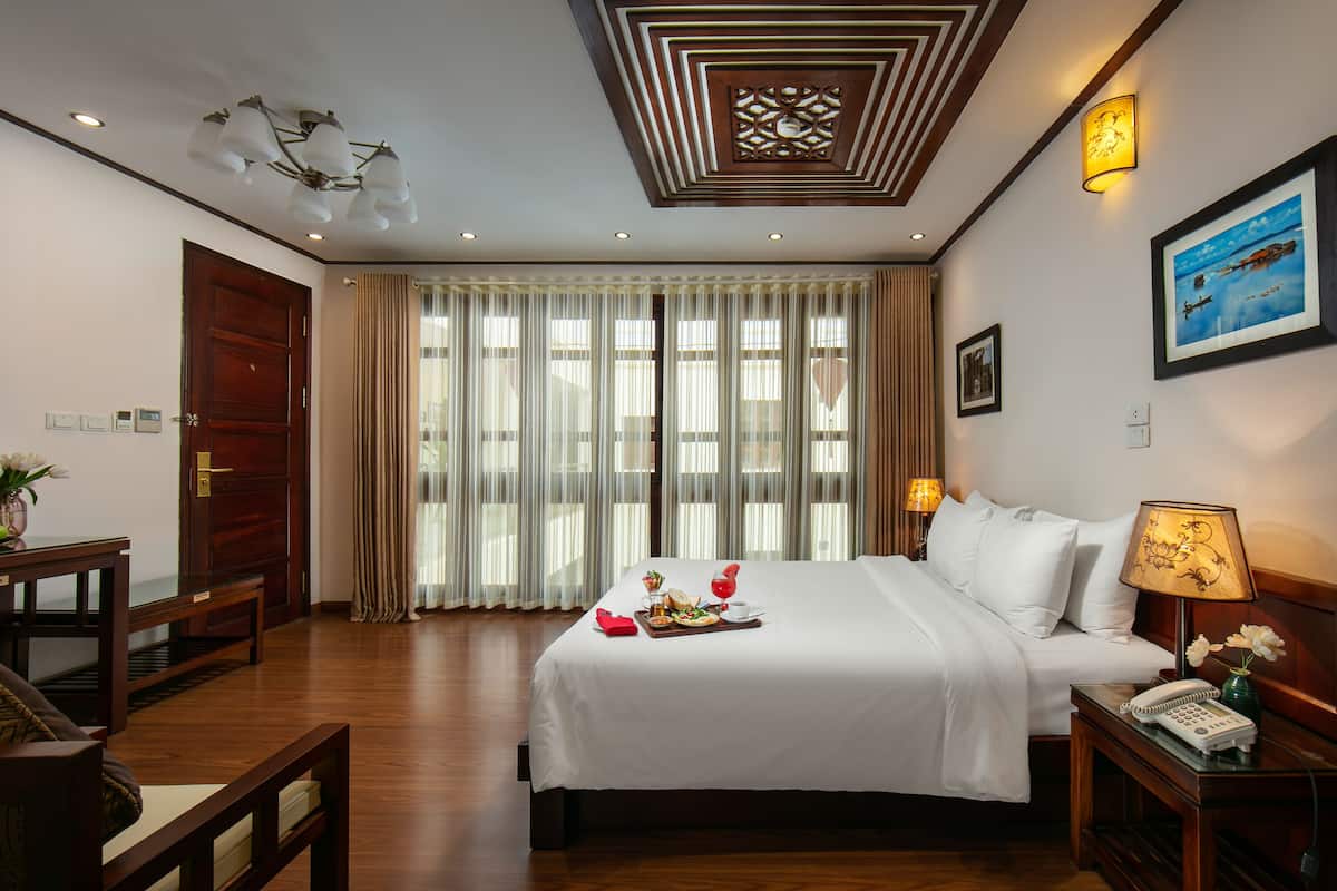 A hotel room with a large bed, a bedside table with a lamp, a wooden nightstand, and a framed picture on the wall.