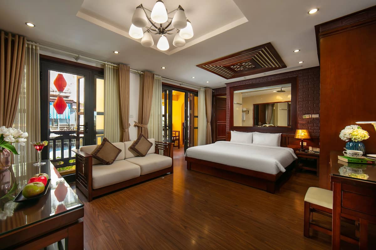 A hotel room with a large bed, a sofa, a desk, and a mirror.