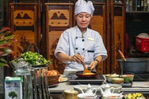 A chef preparing food in a kitchen with various cooking utensils and ingredients. - Hanoi Nostalgia Hotel & Spa (Hanoi)