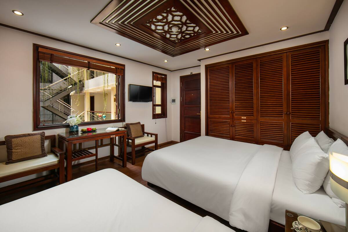 A hotel room with two beds, a desk with a chair, a TV, and a large wardrobe.
