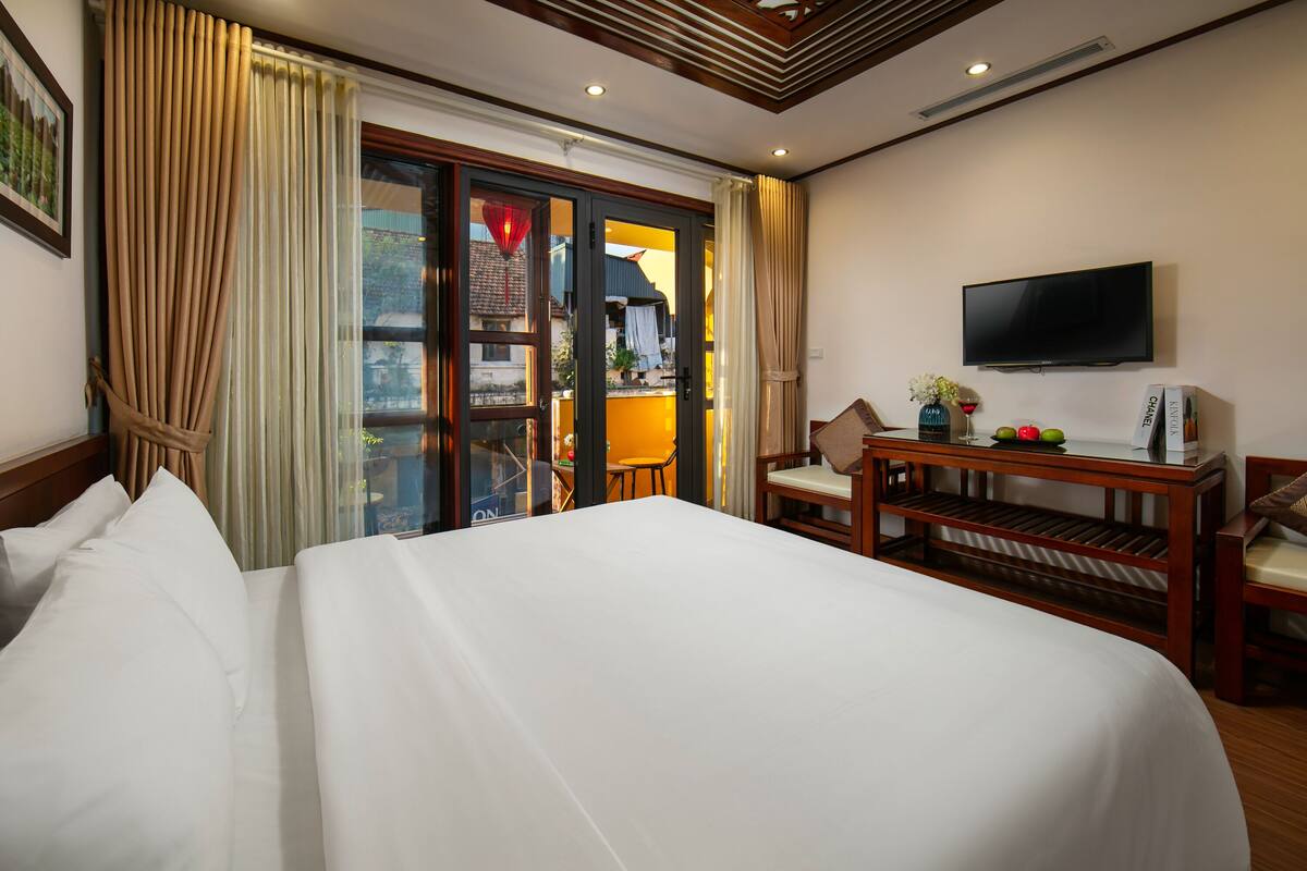 A hotel room with a large bed, a television, a wooden desk, and a view through a glass door.