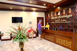 A reception area with a wooden reception desk, a potted plant, and a television mounted on the wall.