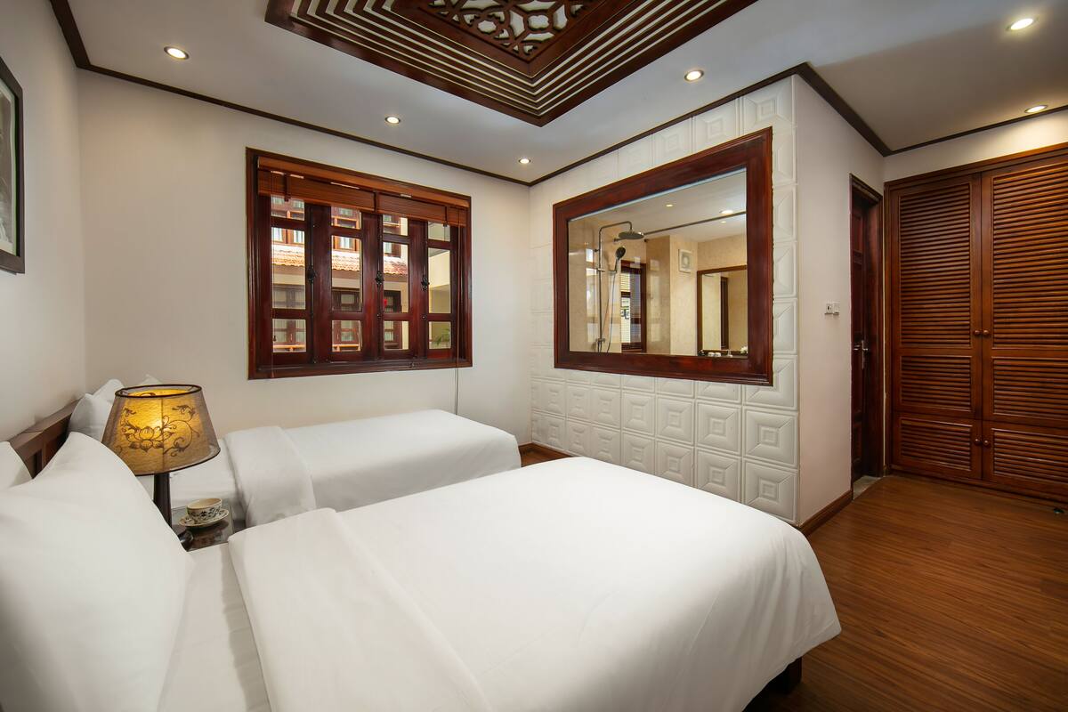 A hotel room with two beds, a wooden ceiling, a large mirror, and a wardrobe.