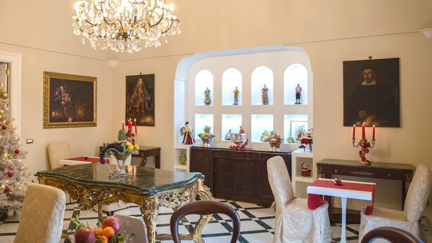 A formal dining room with a chandelier, a Christmas tree, and a collection of framed artworks. - Relais La Rupe (Sorrento)
