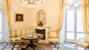 A room with a checkered floor, a round table, a sofa, a chair, a fireplace, a mirror, and a chandelier. - Relais La Rupe (Sorrento)