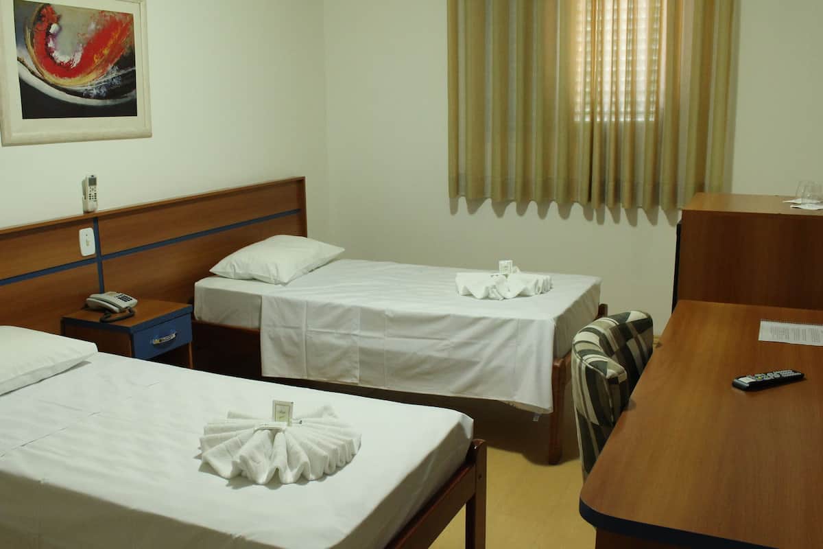 A hotel room with two single beds, a wooden desk, a telephone, and a window with curtains.