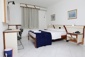 Una habitación de hotel con cama, escritorio, silla y una mesita de noche con lámpara.