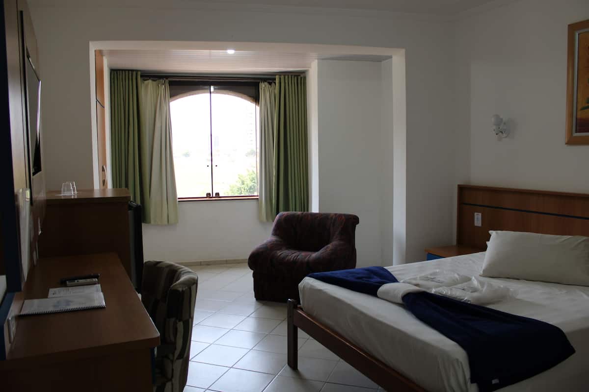 A hotel room with a bed, a desk, a chair, and a window with curtains.