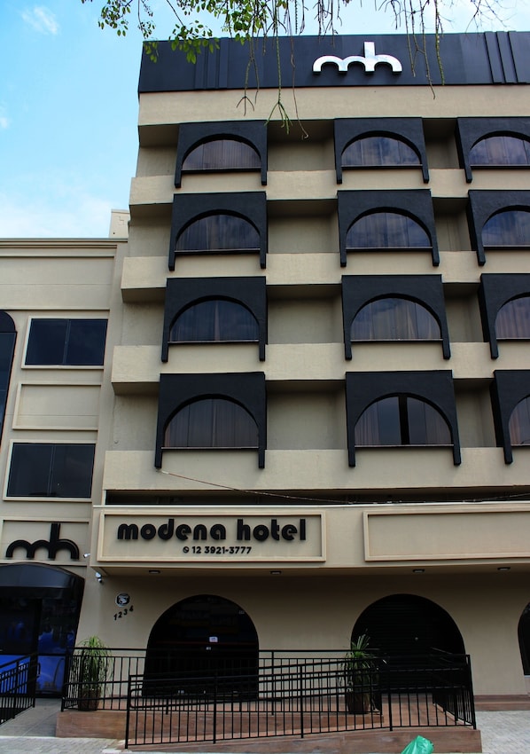 Fachada de hotel con diseño moderno, que presenta ventanas arqueadas y un logotipo destacado en la parte superior.