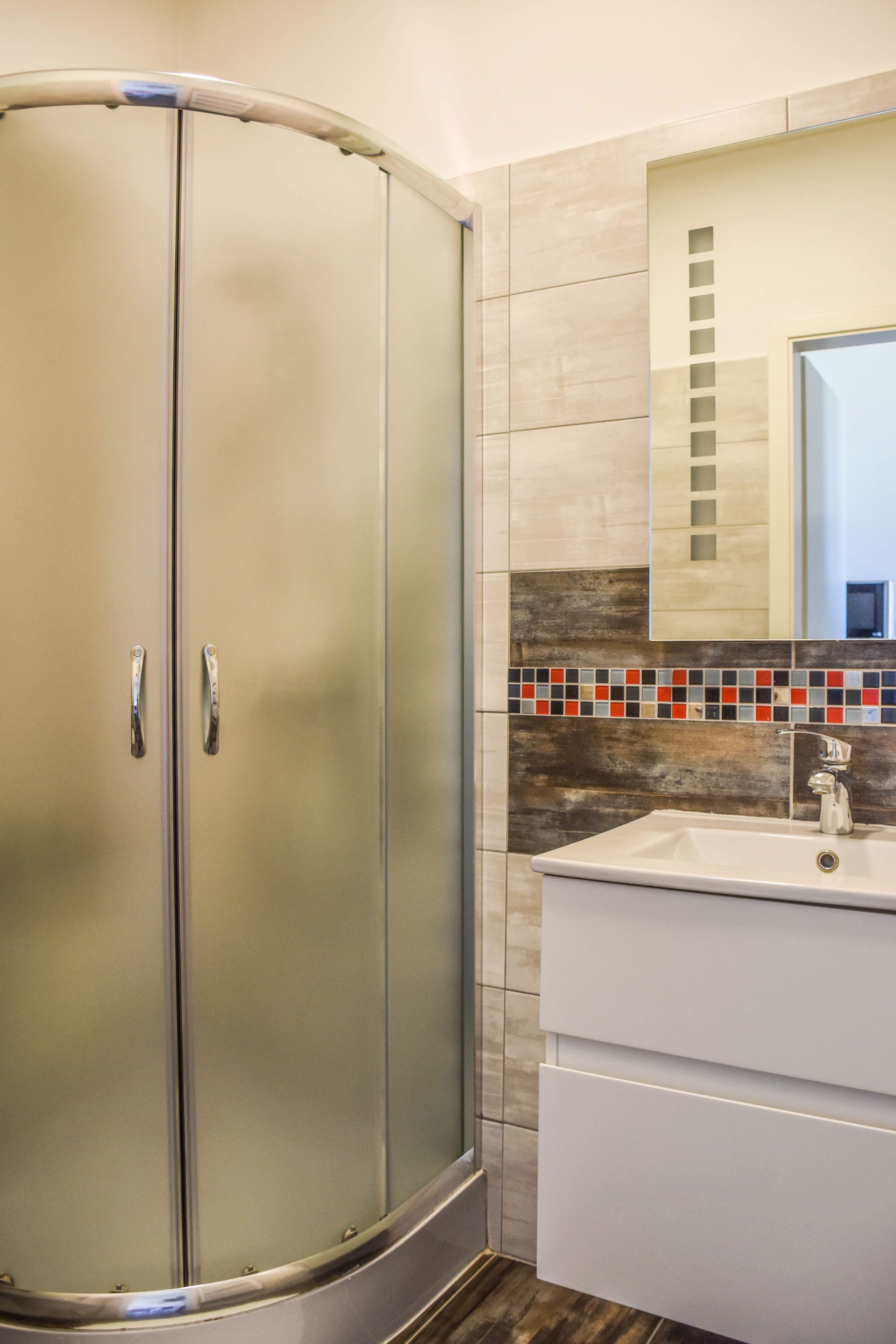 A bathroom with a glass-enclosed shower, a white sink, and a tiled backsplash.