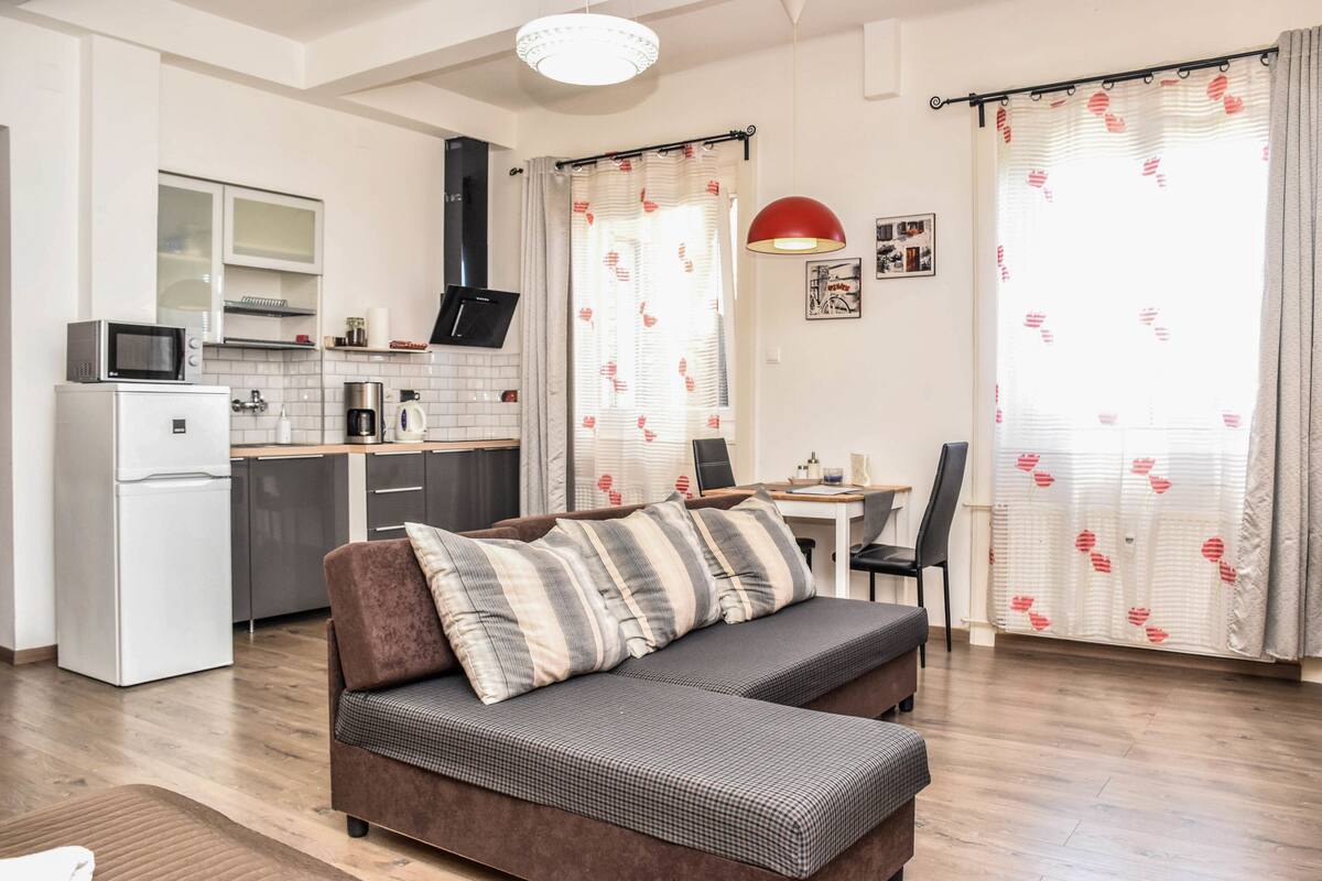 A modern living room with a sofa, a dining area, and a kitchen.