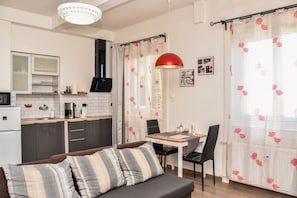 Kompakti oleskelutila, jossa on pieni keittiö, ruokailualue ja raidallisin koristetyynyin varustettu sohva.