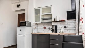 A compact kitchen with a white refrigerator, a microwave, a coffee maker, and a kettle. There is a wooden table and a black chair. - Diamond Astoria (Budapest)