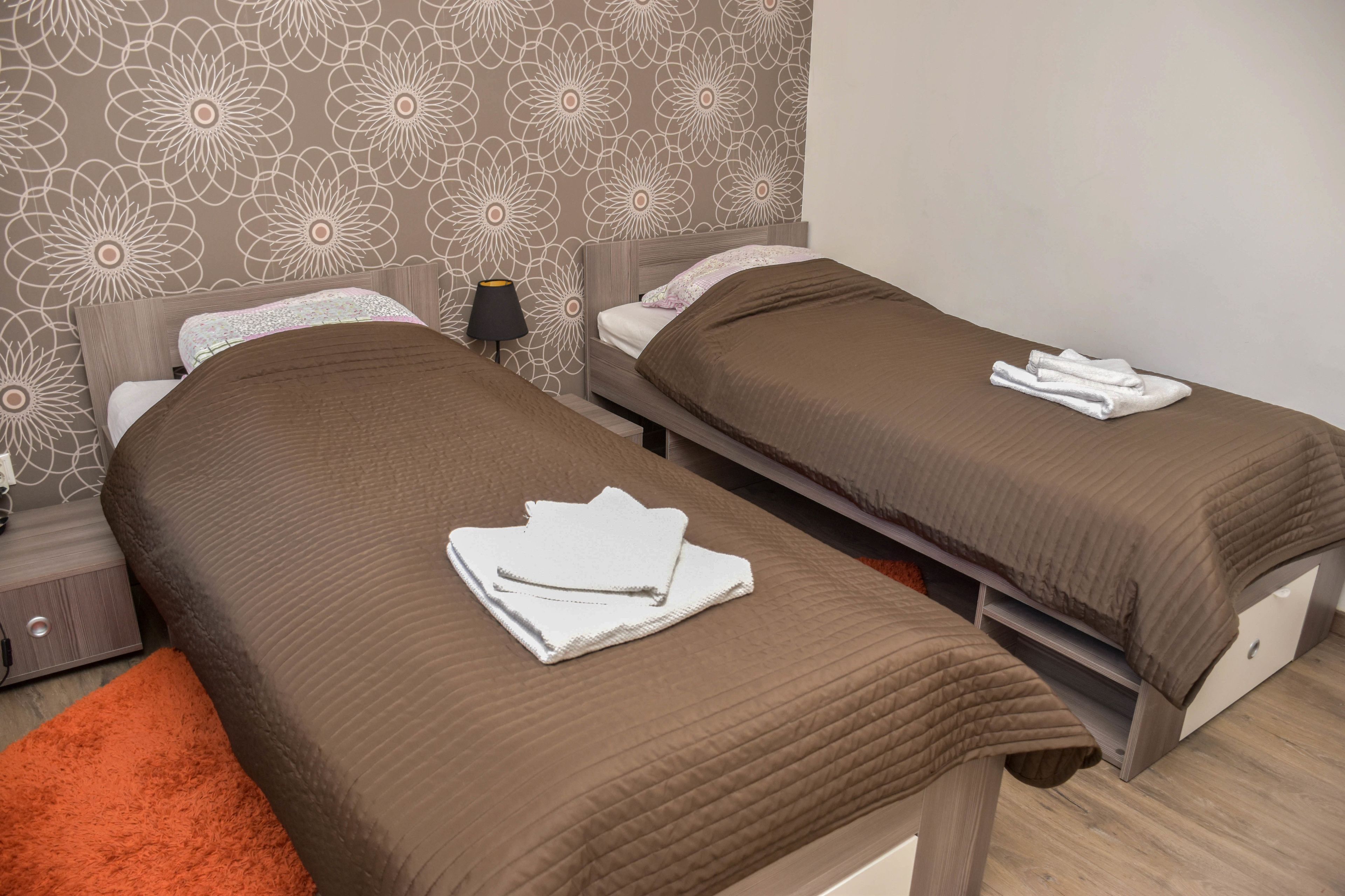 Een hotelkamer met twee enkele bedden, elk met een bruine sprei en witte handdoeken.