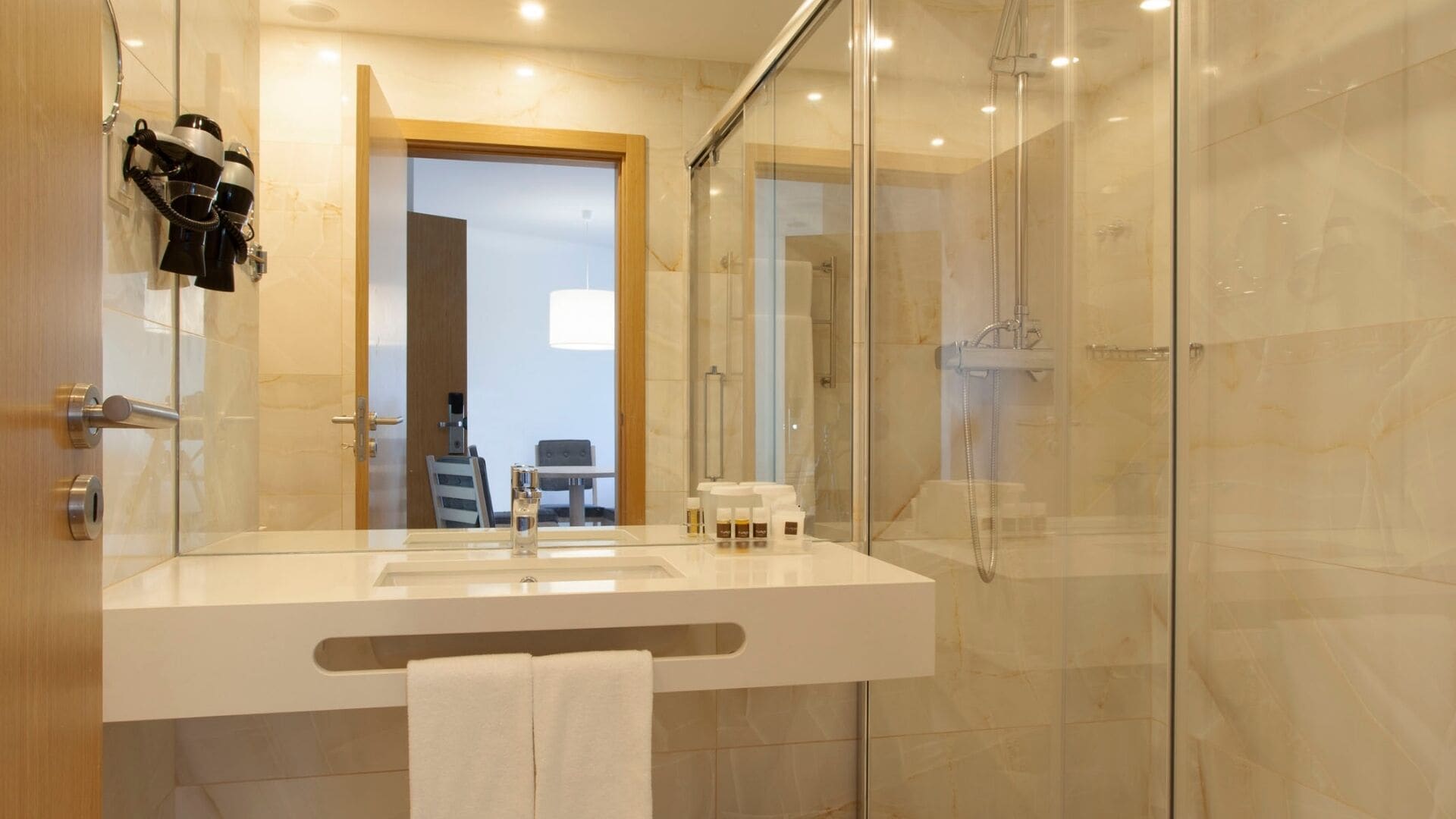 Ein modernes Badezimmer mit Duschkabine aus Glas, Waschbecken mit Handtuch und Haartrockner an der Wand.