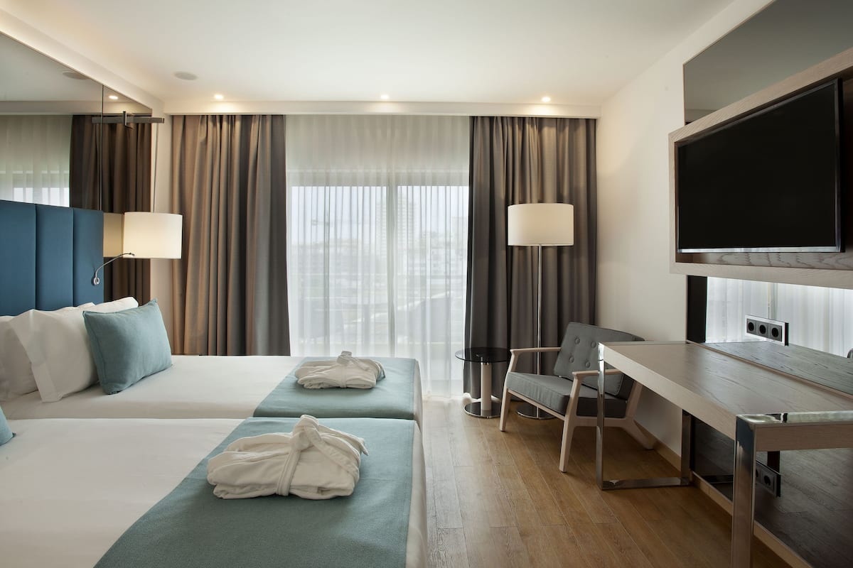 A hotel room with two beds, a desk, a chair, a TV, and a window with curtains.