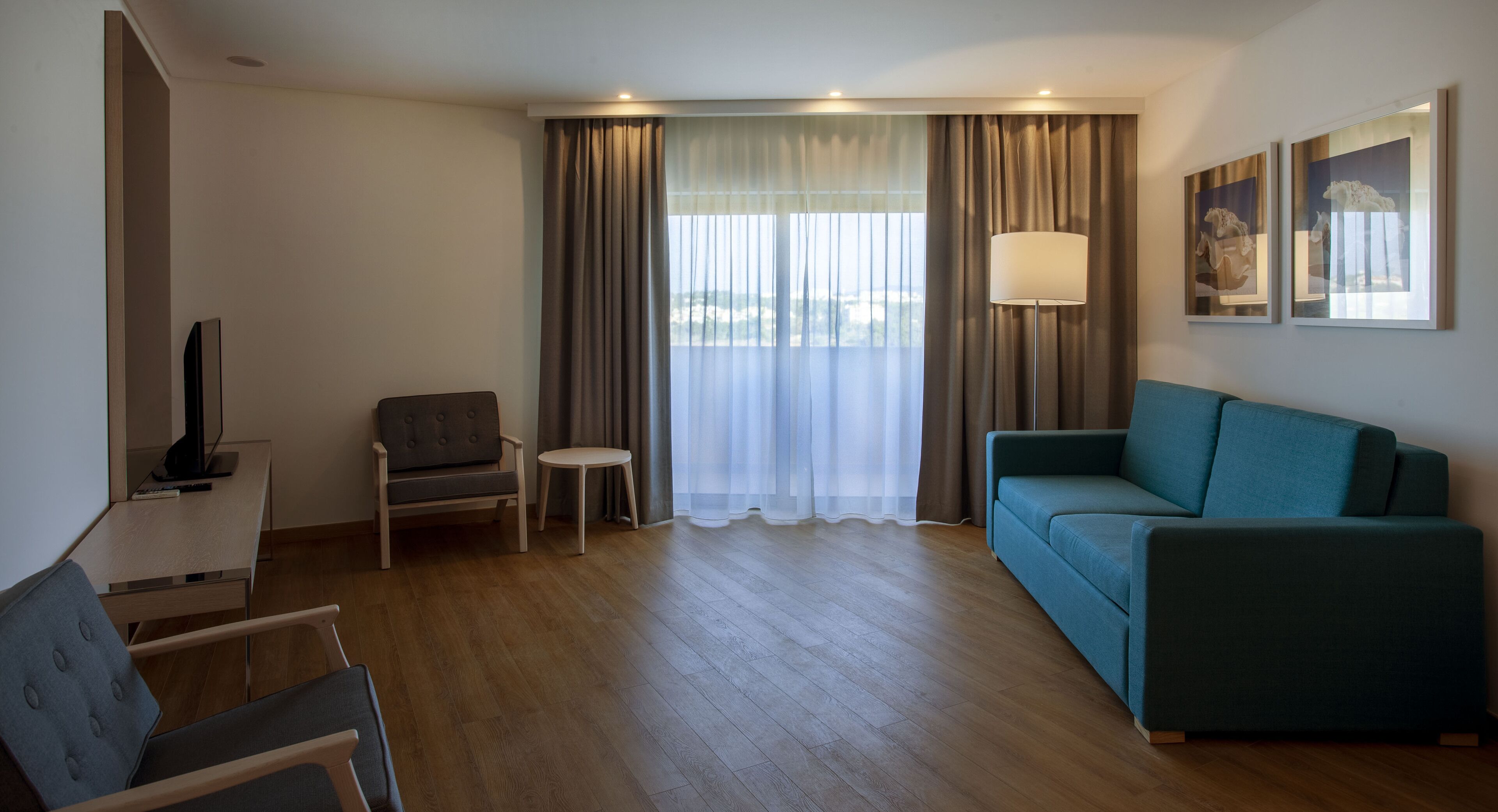 Une chambre d’hôtel moderne équipée d’un canapé, d’un fauteuil, d’une petite table, d’une télévision et d’une lampe.