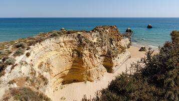 Paisaje costero con un acantilado imponente, una playa de arena y mar azul cristalino.