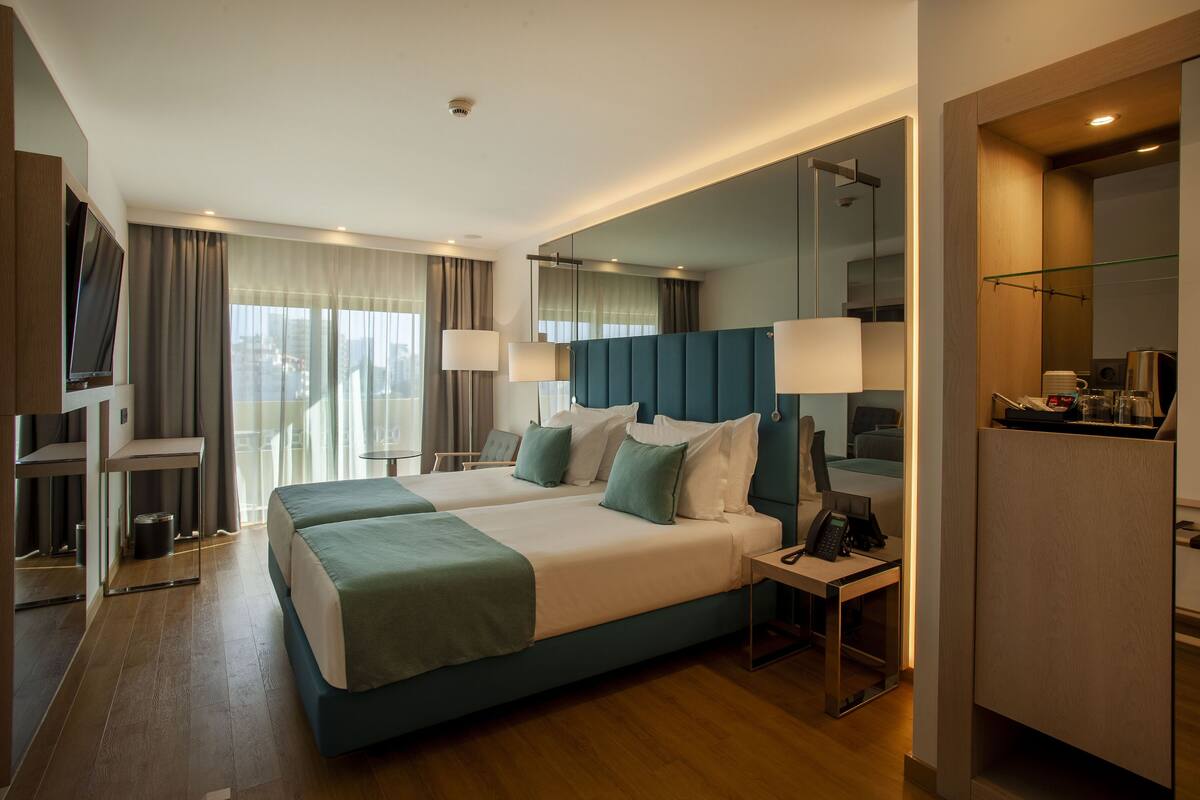 A hotel room with a large bed, bedside tables, a desk, a TV, and a bathroom with a mirror and shower.