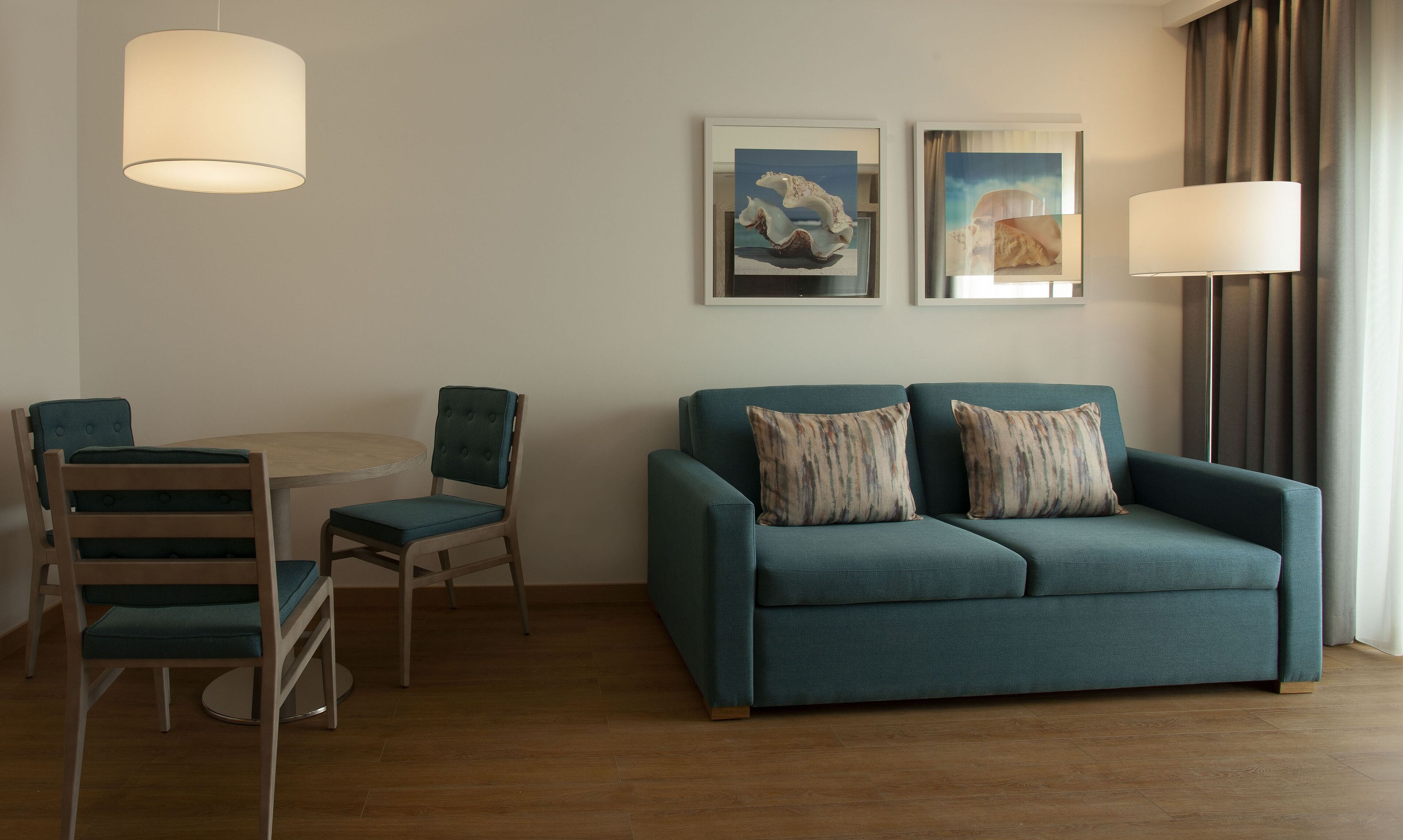 Uma sala de estar moderna com um sofá azul-turquesa, duas poltronas, uma mesa redonda e duas obras de arte emolduradas na parede.