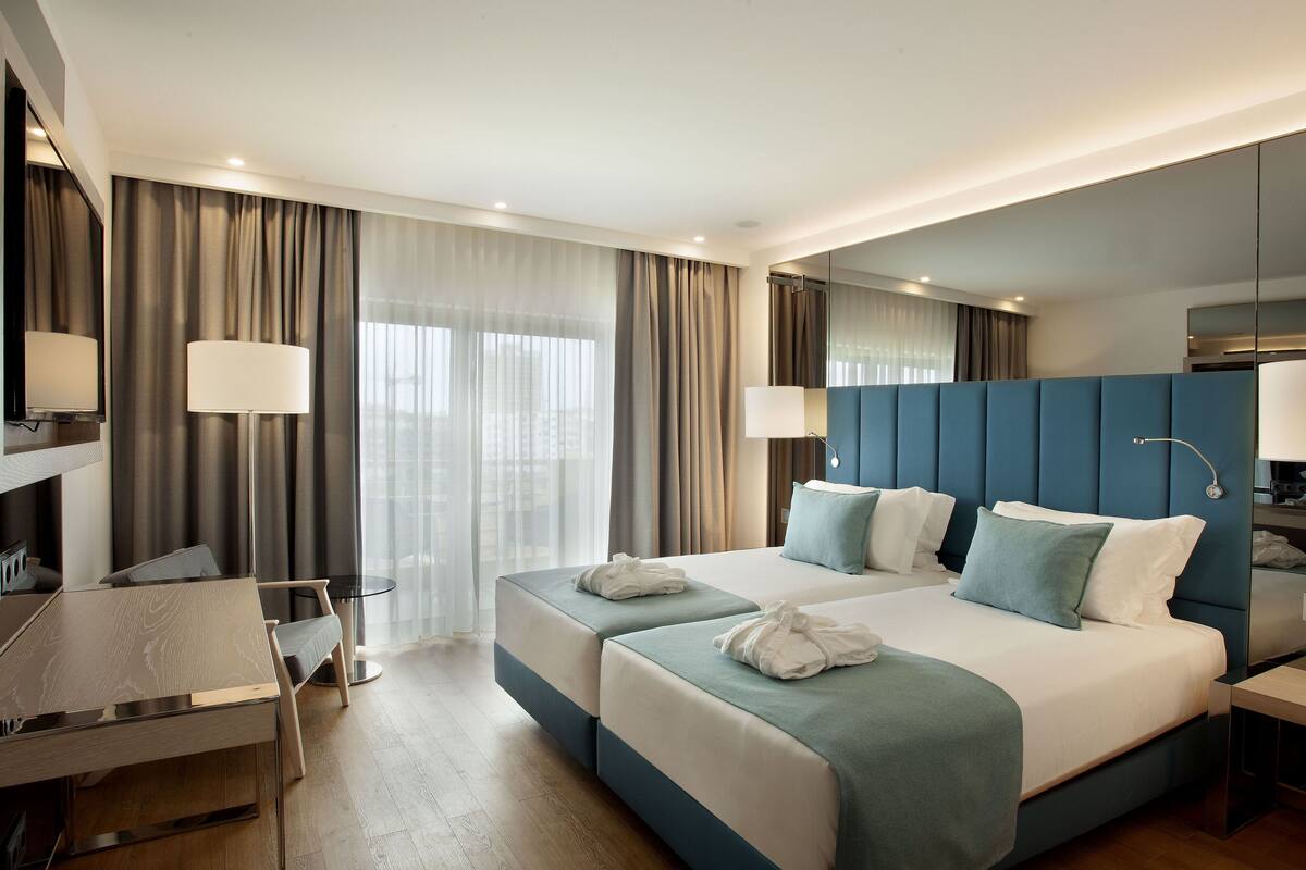 A modern hotel room with two beds, a desk, and a chair.
