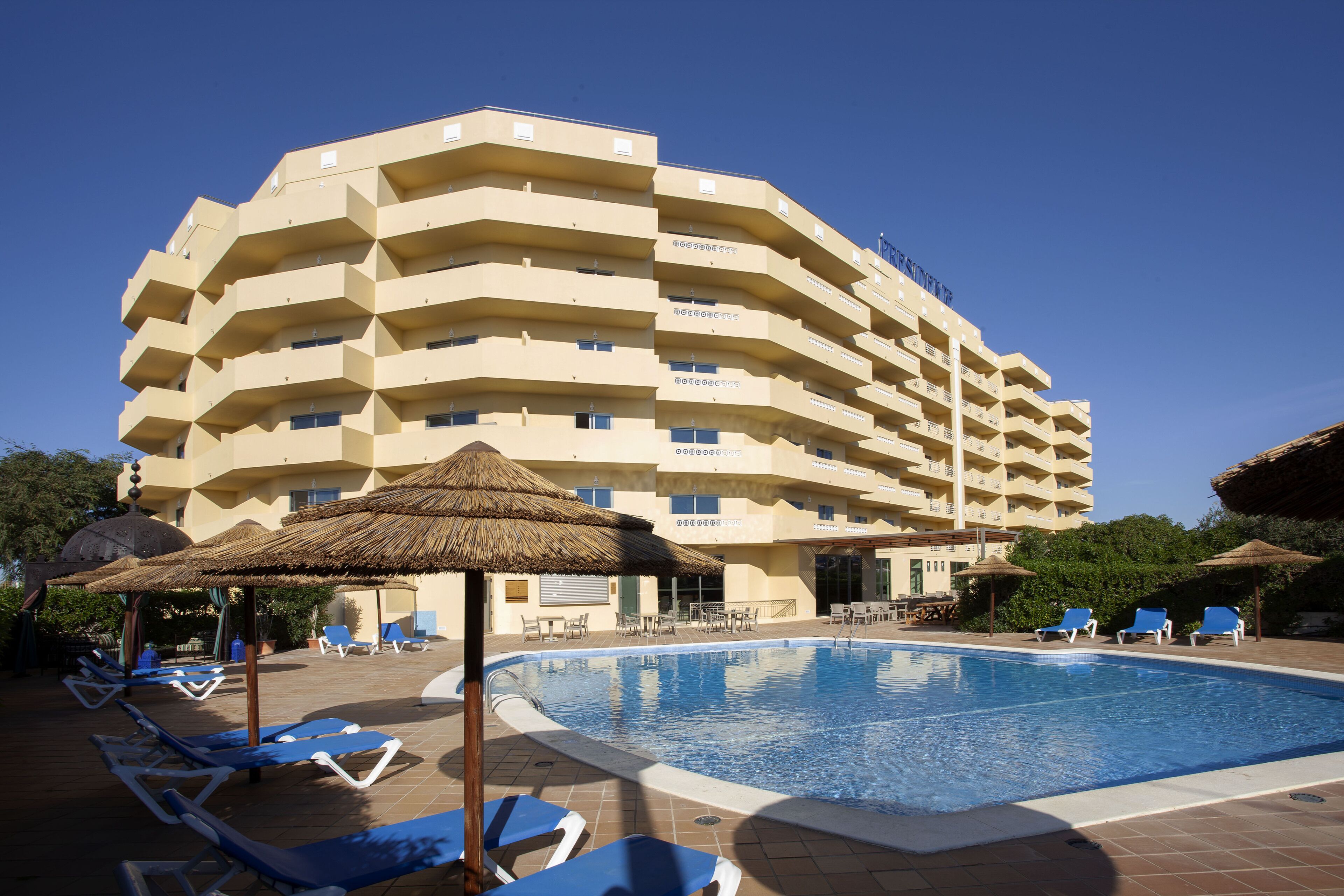 Un hotel con piscina, tumbonas y un toldo de paja.