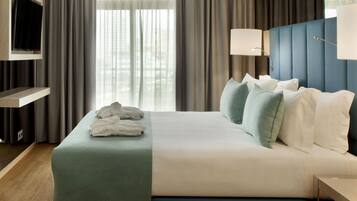 A hotel room with a bed, a TV mounted on the wall, a bedside table, and a window with curtains.