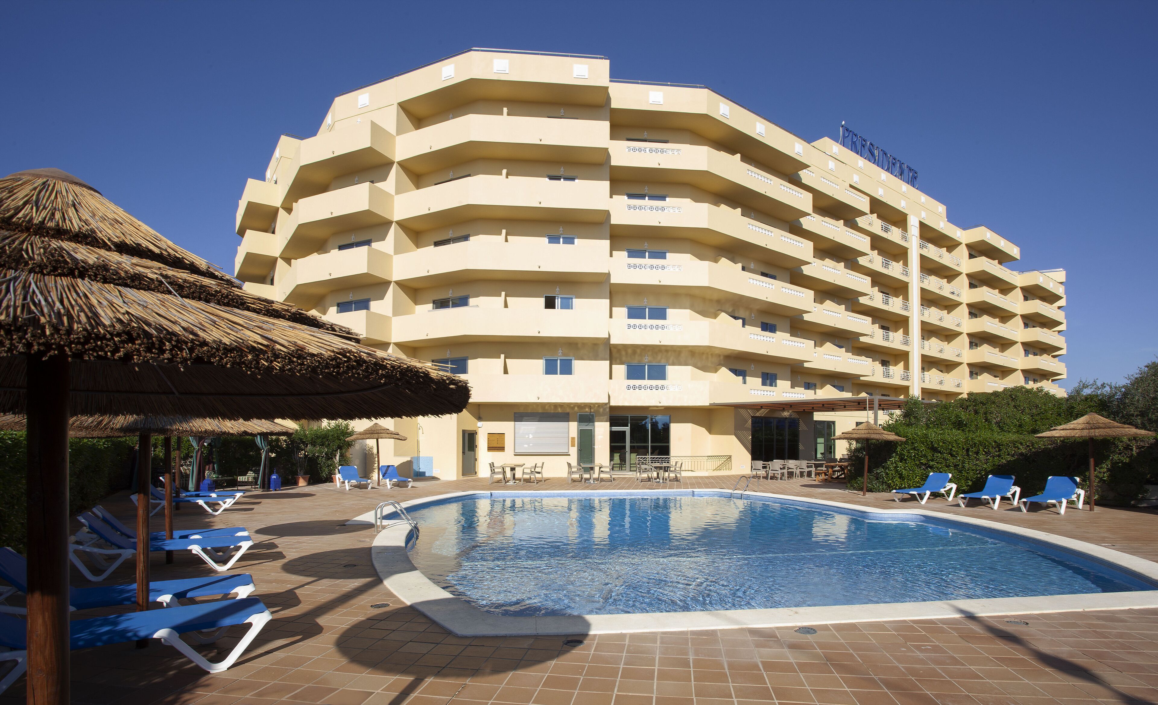 Ein Hotel mit Schwimmbad, Liegestühlen und Strohdachschirmen.