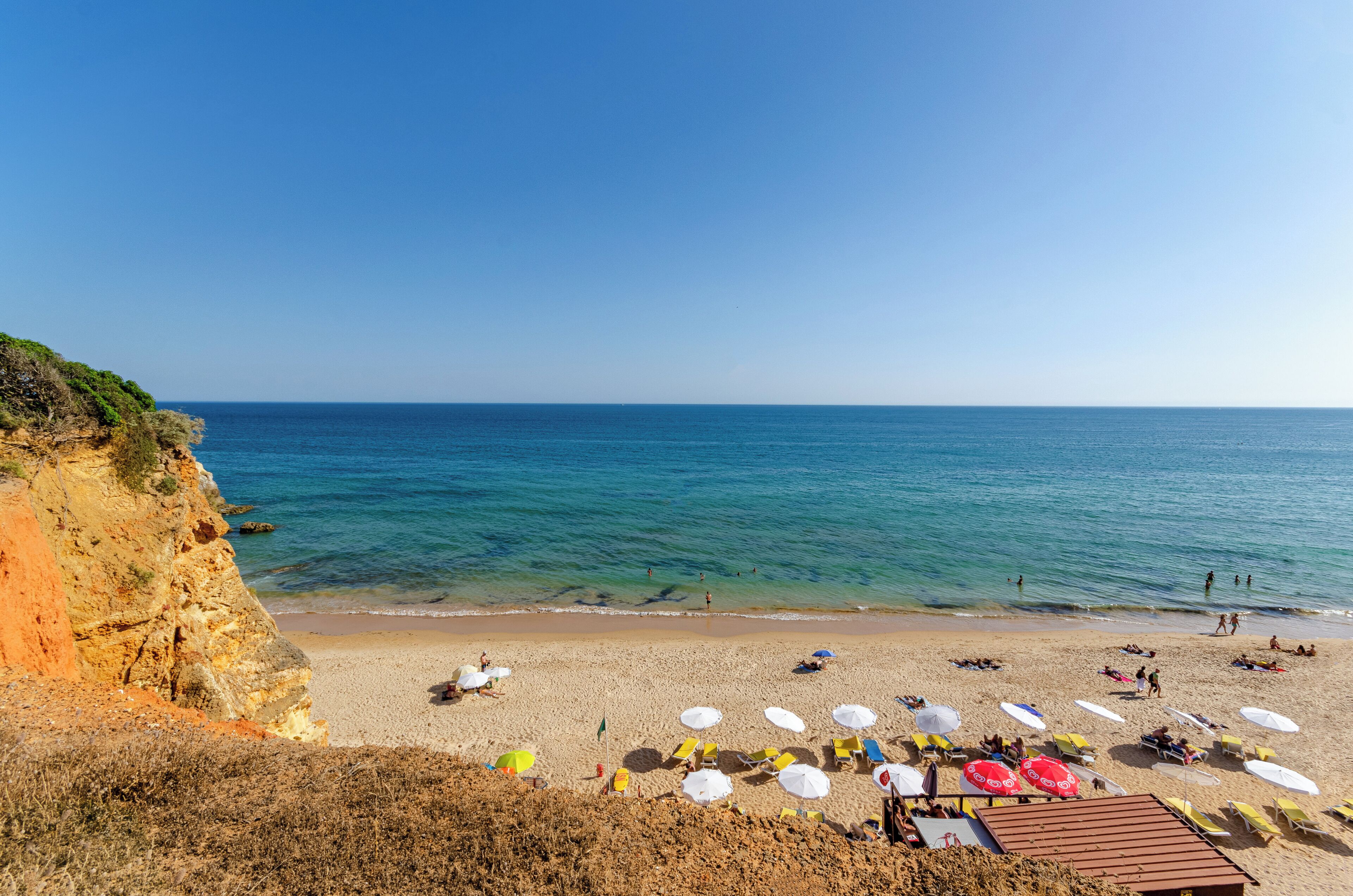 Une plage avec une eau d’un bleu limpide, un rivage sablonneux et des parasols.