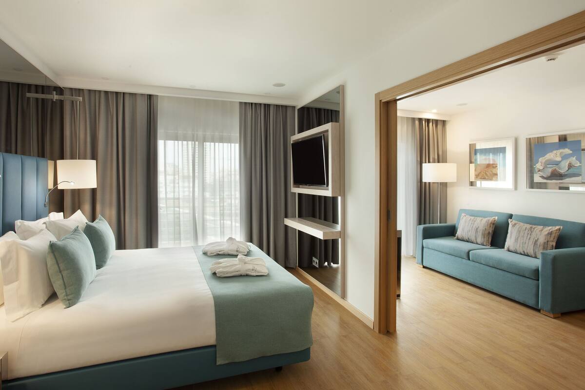 A modern hotel room with a large bed, a TV mounted on the wall, a sofa, and artwork on the walls.