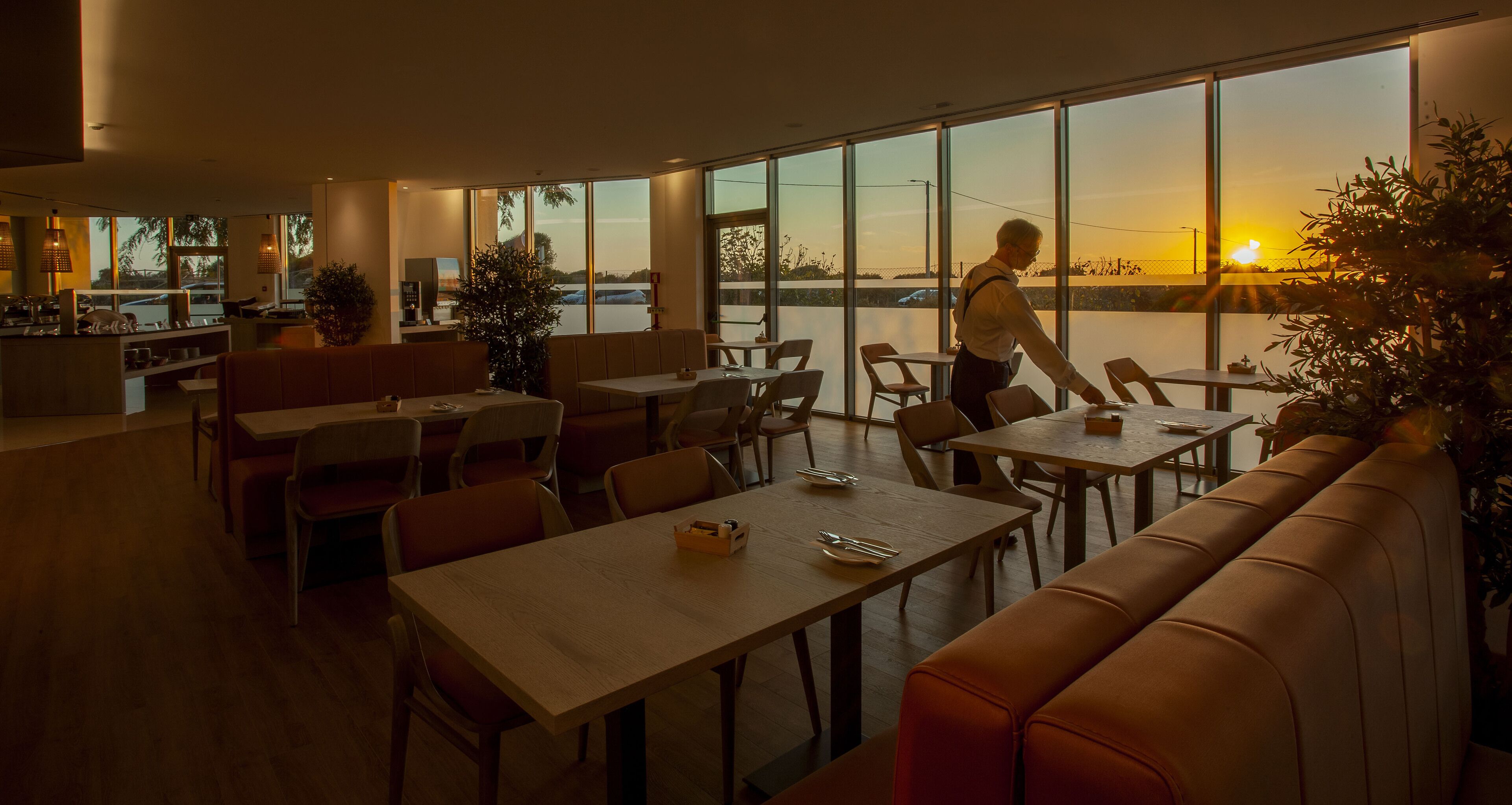 A restaurant with a view of the sunset, tables, chairs, and a bar area.
