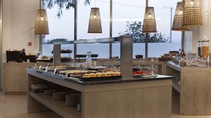 A buffet area with a variety of food items, a coffee station, and a view of the outdoors through large windows. - TURIM Presidente Hotel (Portimão)