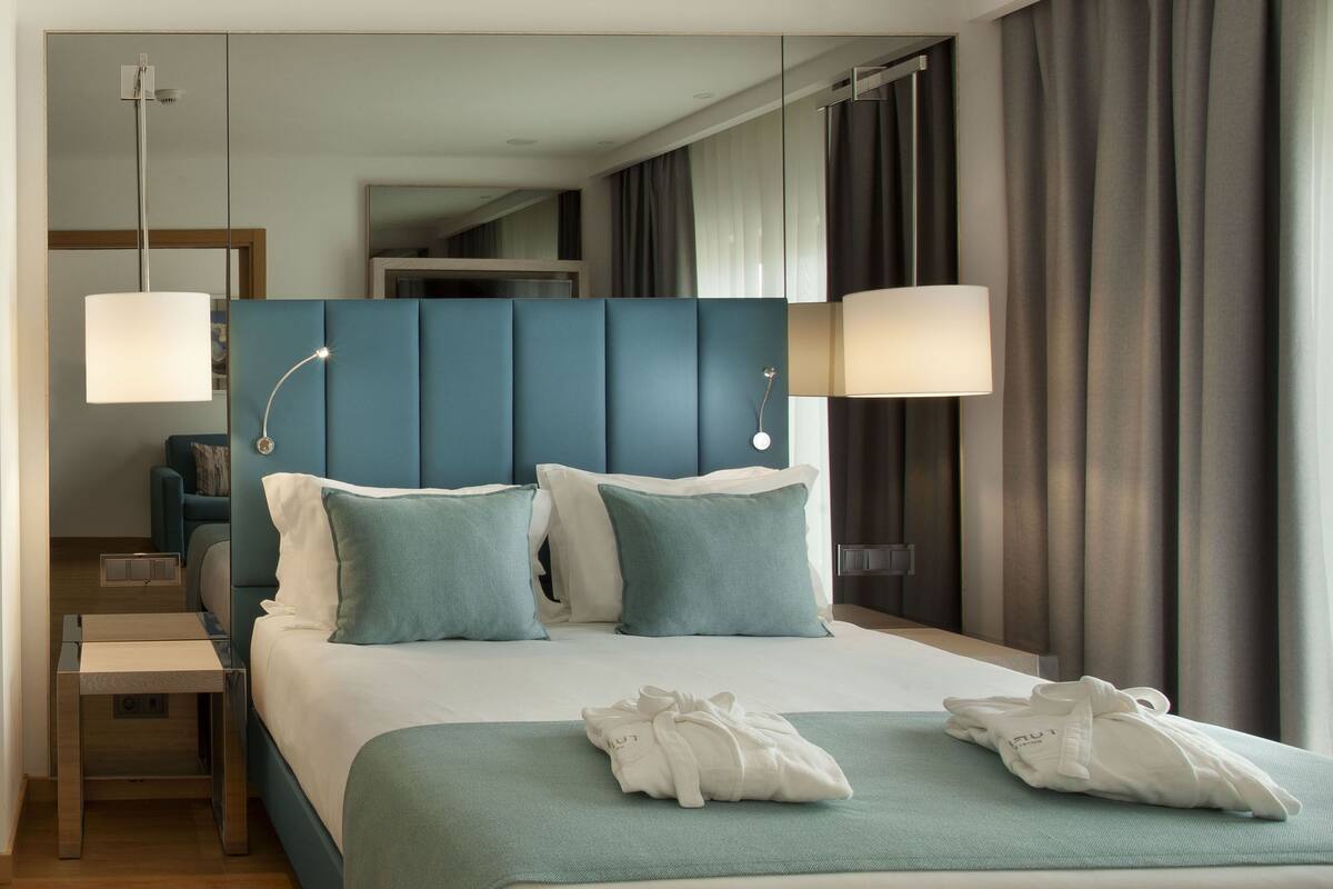 A hotel room with a large bed, two bedside lamps, a nightstand, and a view of the hallway.