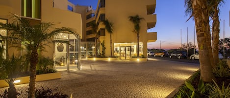 A hotel entrance with a cobblestone driveway, palm trees, and a modern building facade.