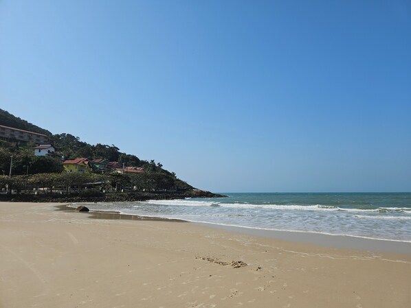 A beach with a clear sky, sandy shore, and buildings on a hillside.