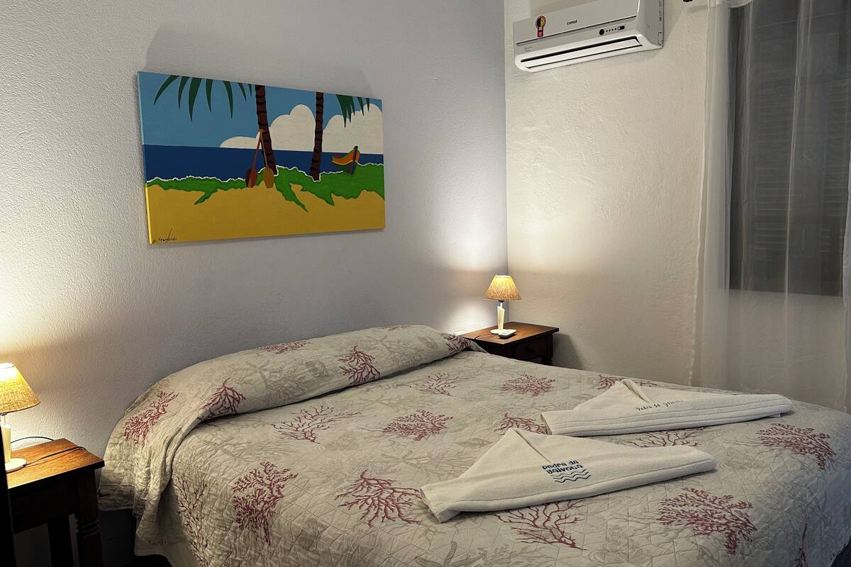 Ein Schlafzimmer mit einem Bett, einem Strandbild, einer Klimaanlage und einer Nachttischlampe.