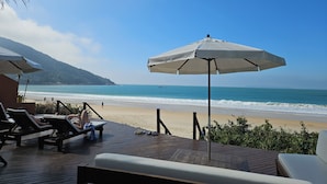 A beachside lounge area with wooden deck, lounge chairs, and umbrellas. - Pousada Pedra da Gaivota (Bombinhas)