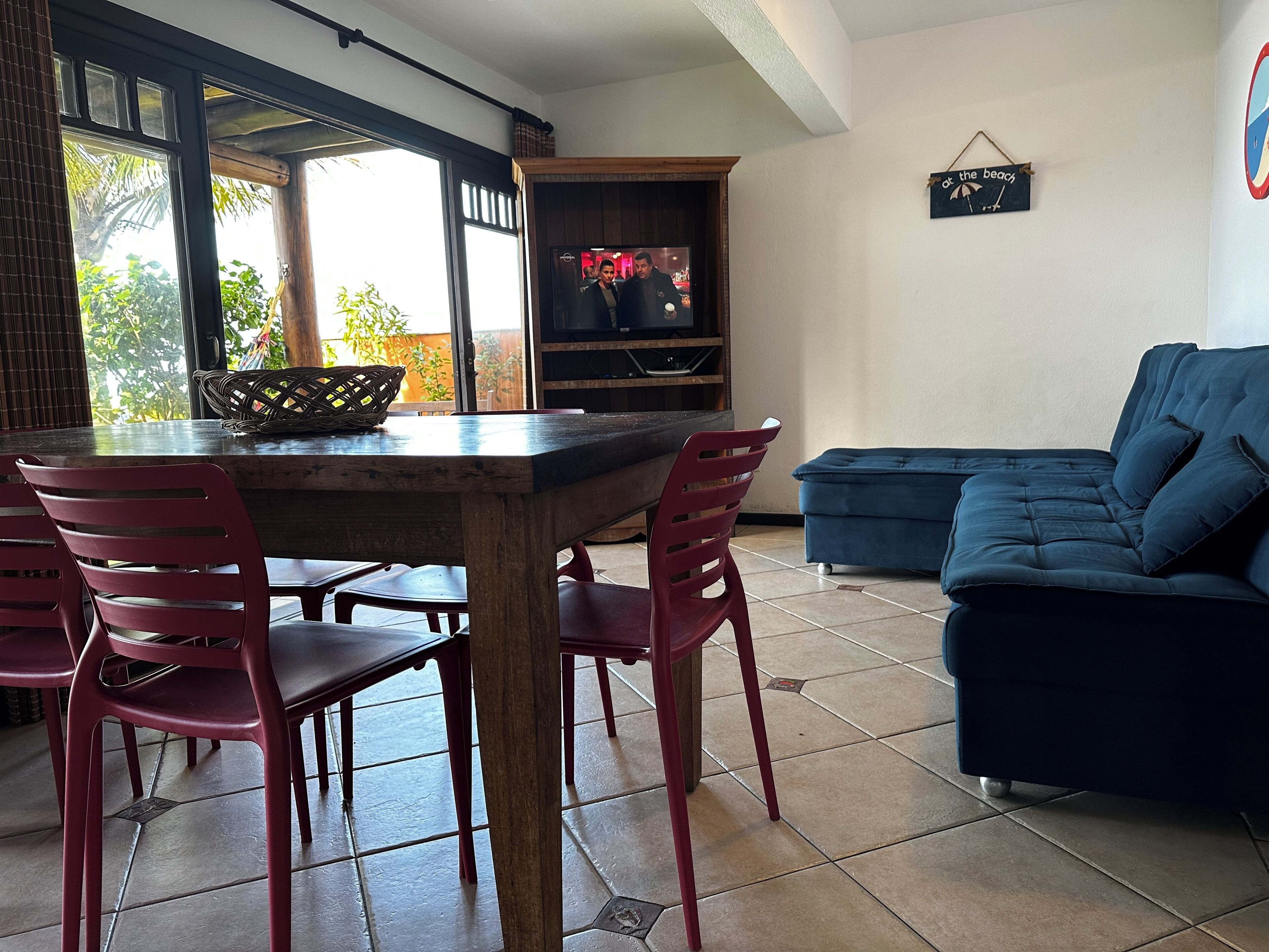 Un área de comedor con una mesa de madera y sillas rojas, un sofá azul y un televisor al fondo.