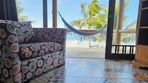 A room with a patterned sofa, a hammock, and a view of the beach and palm trees. - Pousada Pedra da Gaivota (Bombinhas)