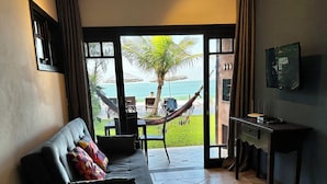 A living room with a sofa, a dining table, and a view of the beach. - Pousada Pedra da Gaivota (Bombinhas)