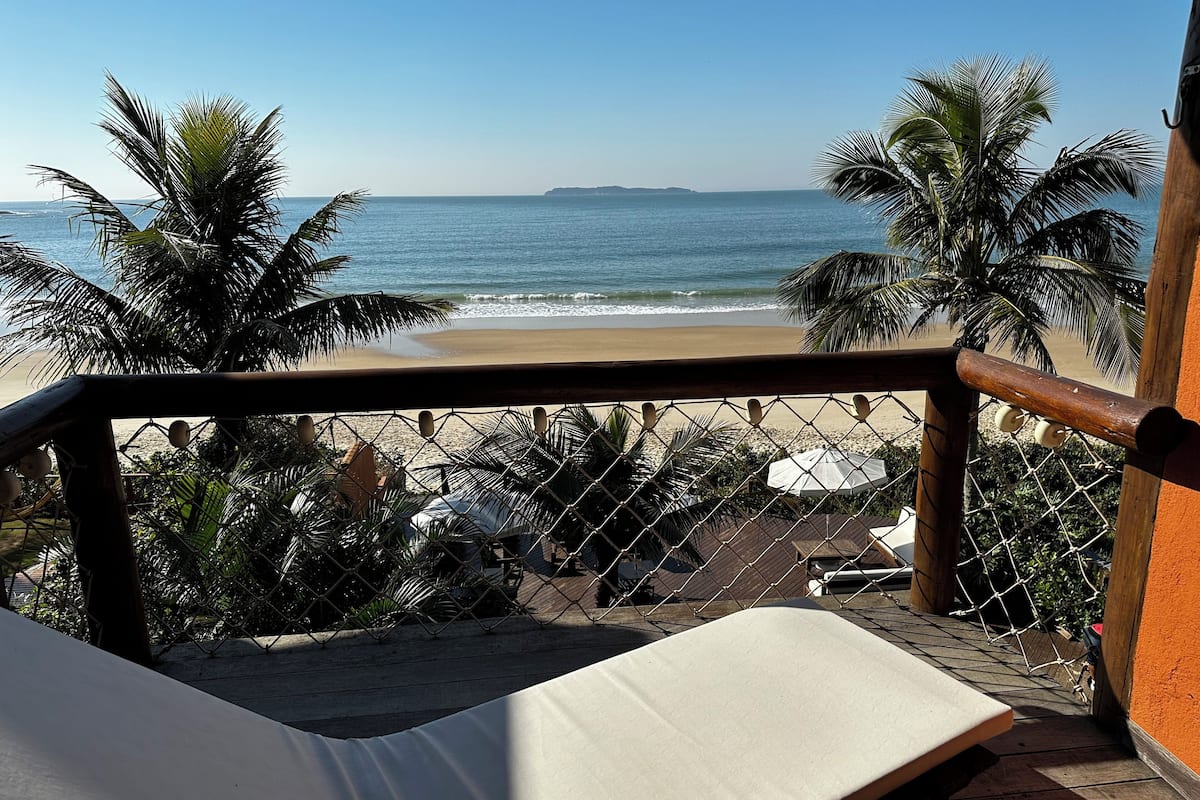 Ein Balkon mit Blick auf den Strand, Palmen und einem Zaun aus Maschendraht.