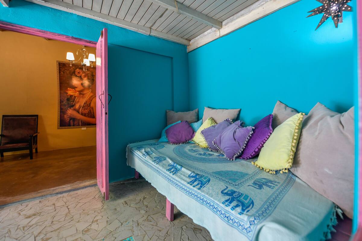 Una habitación con una cama, almohadas coloridas, un cartel en la pared y una silla.