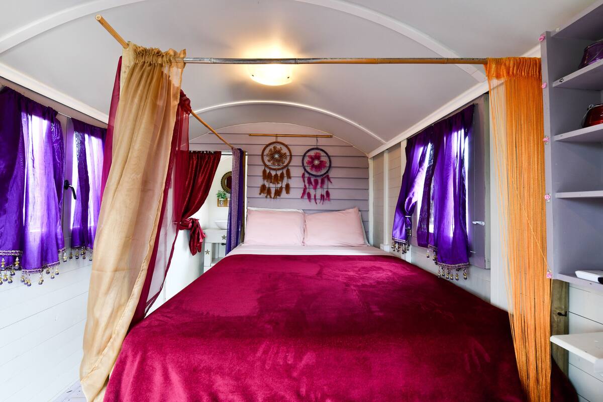 Un dormitorio con una cama grande, cortinas moradas y una lámpara en el techo.