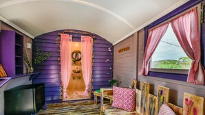 A room with a purple wall, a wooden bench, a television, and a window with pink curtains. - Mammaloes (Santa Cruz)