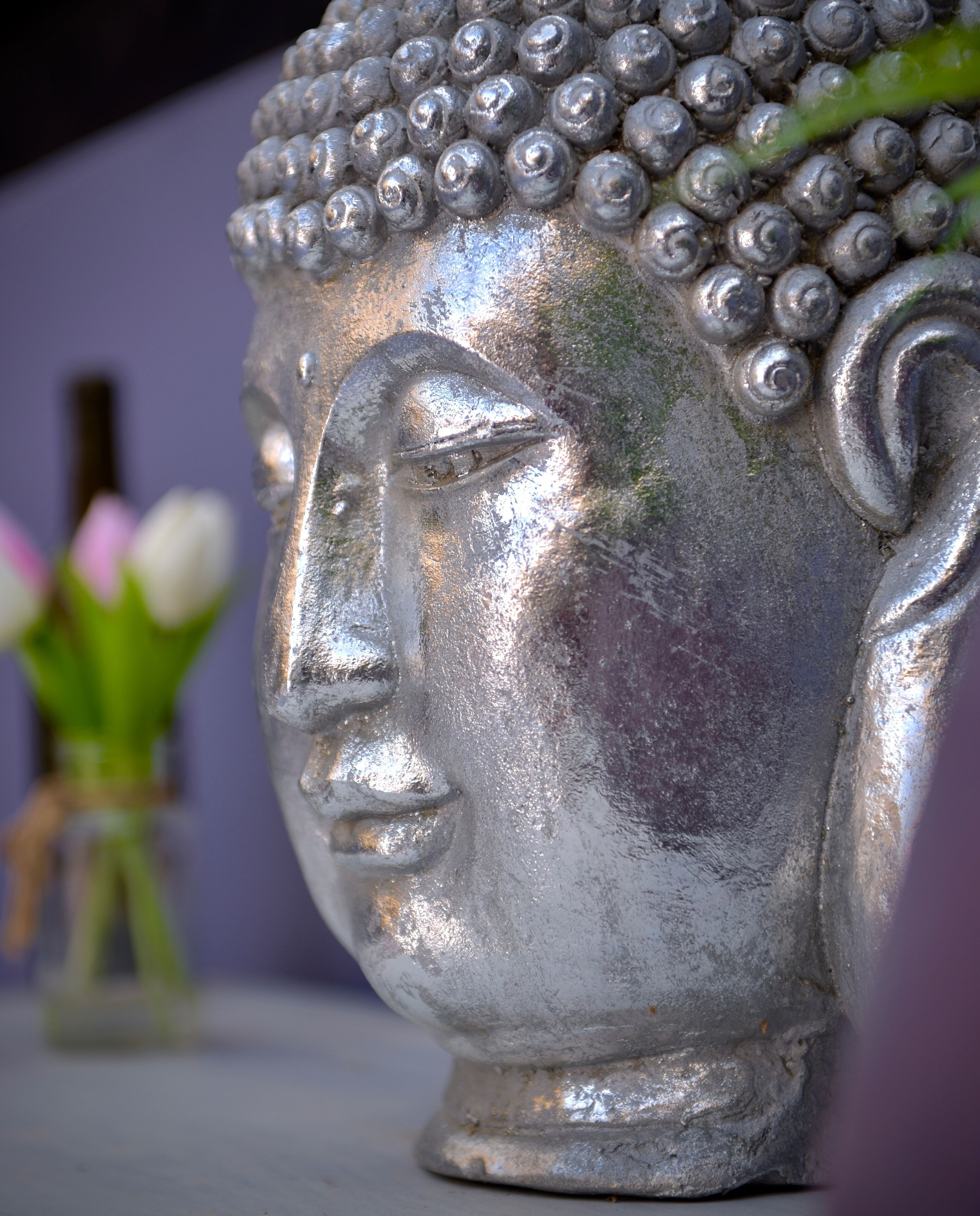Nahaufnahme einer metallenen Buddha-Kopf-Skulptur mit strukturierter Oberfläche und glänzender Reflexion.