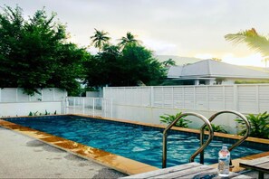 Piscina con barandillas metálicas, rodeada de follaje y una cerca blanca.