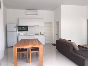 A modern kitchen with white cabinets, a wooden dining table, and a brown sofa in a bright living area.