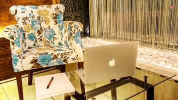 A laptop on a glass table with a floral armchair and a pen on a paper beside it.