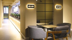 Ein modernes Interieur mit einer Rezeption, zwei Sitzbereichen mit Stühlen und Tischen sowie beleuchteten Kontaktdaten an der Wand.
